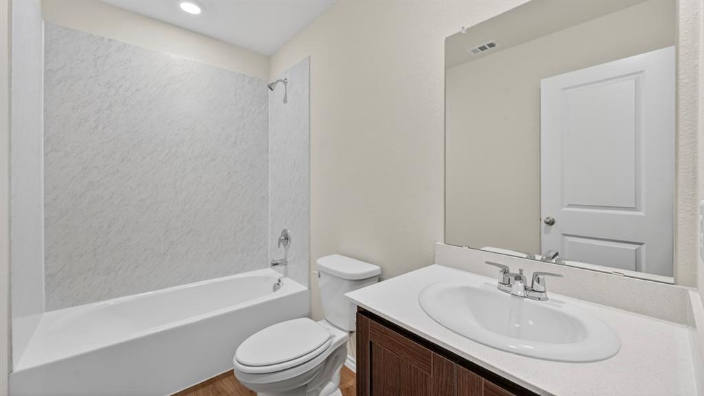 White bathtub with a textured shower surround, vanity with an integrated sink and light-toned countertop, dark wood-finish cabinet, and a large wall-mounted mirror