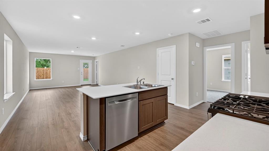 Open-concept living space featuring wood-finish flooring, recessed lighting, and an island with an integrated stainless steel sink and dishwasher Open-concept living space featuring wood-finish flooring, recessed lighting, and an island with an integrated stainless steel sink and dishwasher