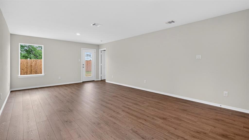 Spacious room featuring wood-finish flooring, neutral-toned walls, a bright window, and a glass-paneled door