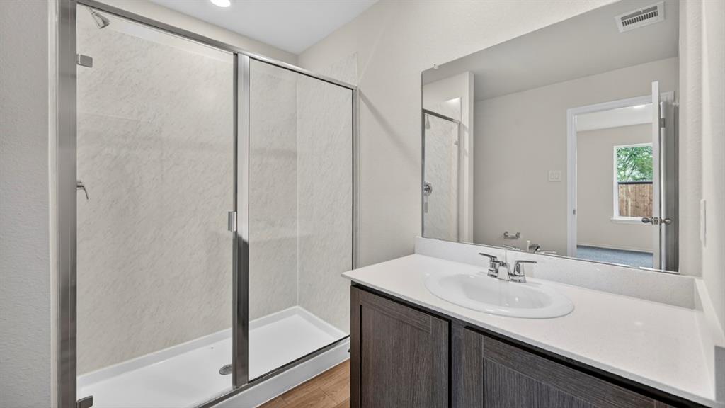 Walk-in shower with sliding glass door, single vanity with integrated sink, quartz-finish countertop, and wood-finish cabinetry