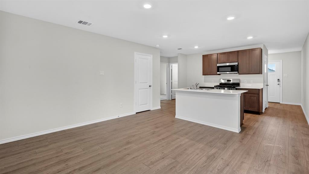Open-concept living space featuring wood-finish flooring, recessed lighting, a kitchen island with a white countertop, and dark wood cabinetry Open-concept living space featuring wood-finish flooring, recessed lighting, a kitchen island with a white countertop, and dark wood cabinetry