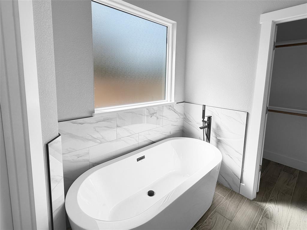 Freestanding soaking tub with matte black fixtures, large-format tile surround, frosted privacy window, and wood-finish flooring