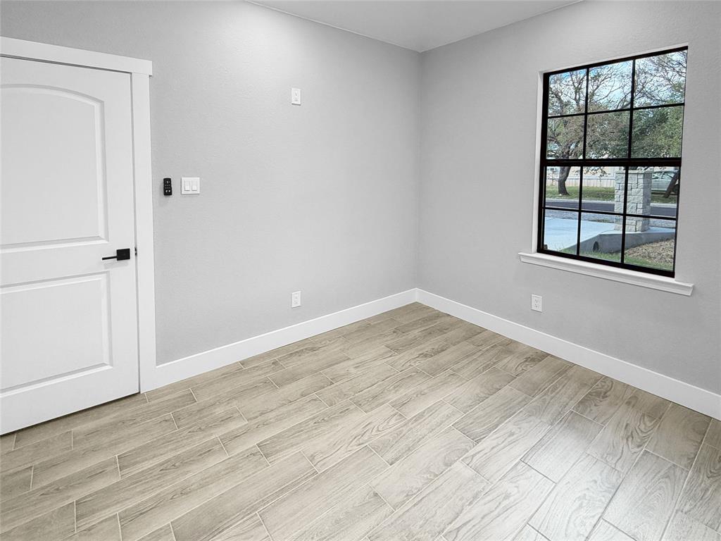 Wood-finish flooring, neutral wall tones, multi-pane window with black framing, and a white arched-panel door with matte black hardware
