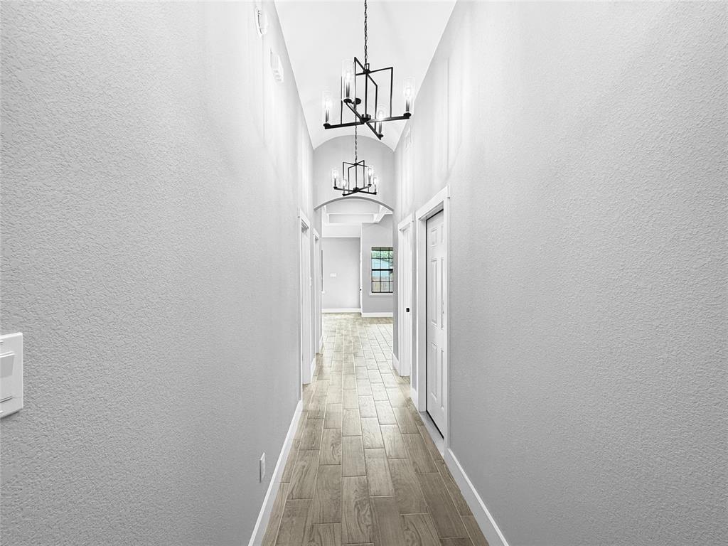 Hallway featuring a barrel-vaulted ceiling, wood-finish flooring, and dual geometric-frame chandeliers Hallway featuring a barrel-vaulted ceiling, wood-finish flooring, and dual geometric-frame chandeliers
