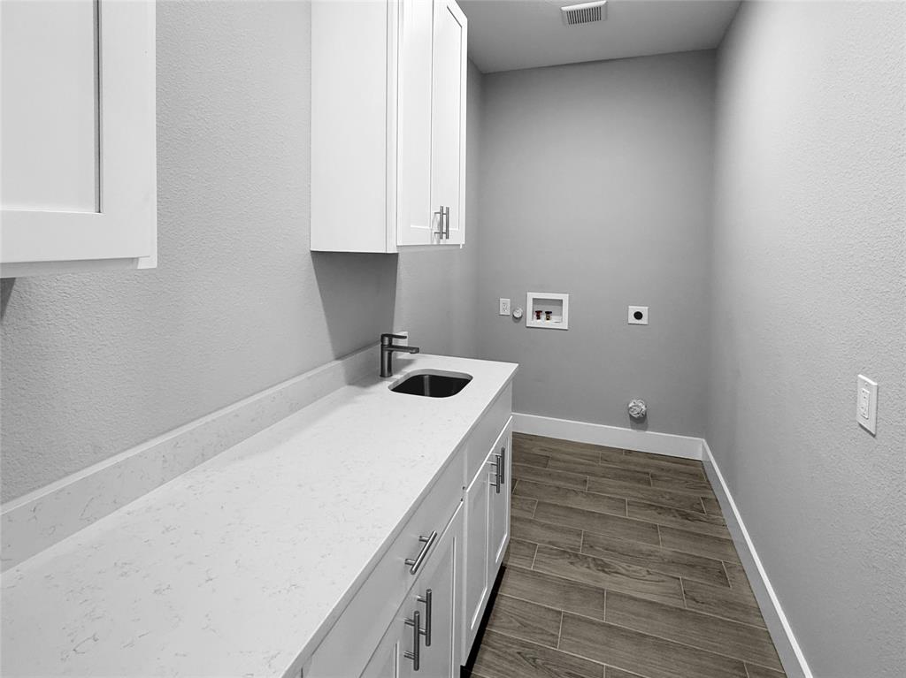 Utility space featuring white shaker-style cabinetry, solid-surface countertop, undermount sink with metal faucet, and wood-finish tile flooring