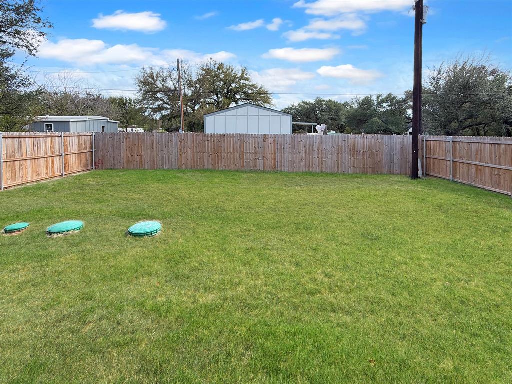 Level grassy backyard featuring a wood privacy fence and mature trees