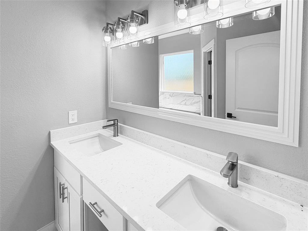 Dual-sink vanity featuring a white composite countertop, undermount basins, brushed nickel hardware, and a framed mirror with integrated multi-bulb lighting