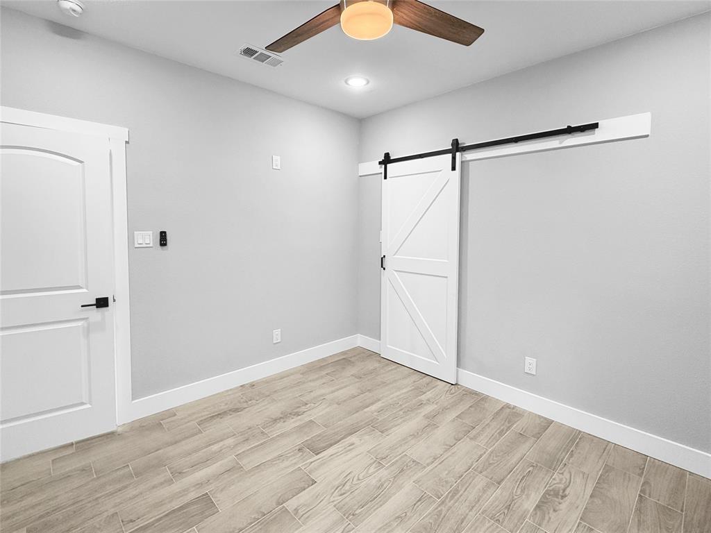 Interior space featuring wood-finish tile flooring, a white paneled sliding barn door with matte black hardware, and a ceiling fan with integrated lighting