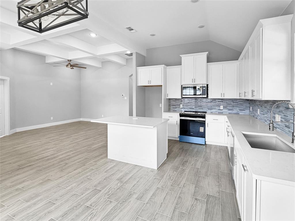 Kitchen featuring white cabinetry, quartz countertops, a tiled backsplash, wood-finish flooring, and a coffered ceiling with a geometric pendant light Kitchen featuring white cabinetry, quartz countertops, a tiled backsplash, wood-finish flooring, and a coffered ceiling with a geometric pendant light