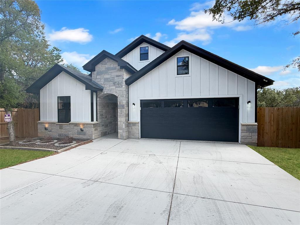Modern exterior featuring a white vertical siding facade, masonry stone veneer accents, multi-gabled roofline, and a multi-car garage with glass-panel detailing