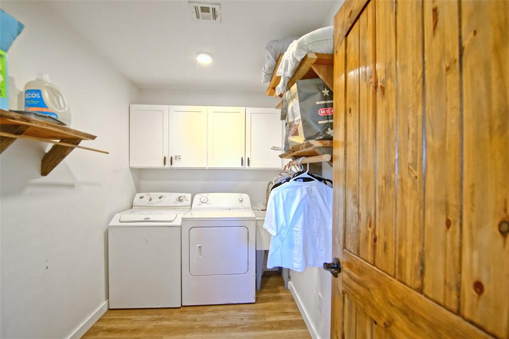 Laundry space featuring wood-finish flooring, white cabinetry, open wooden shelving, and a natural wood door
