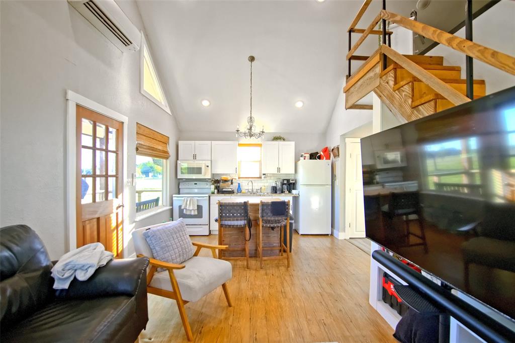 Vaulted ceilings with recessed lighting, wood-finish flooring, white kitchen cabinetry, and an open timber staircase