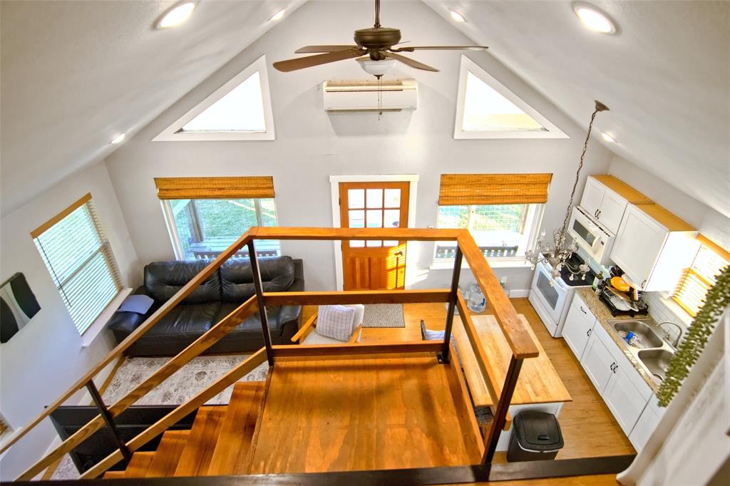 Vaulted ceiling with a ceiling fan, recessed lighting, wood-finish stairs with a wooden railing, multi-pane entry door, and white cabinetry