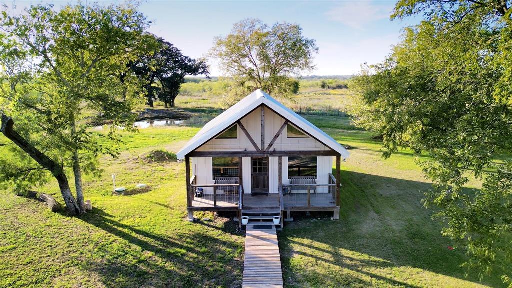 Gable-roof cottage featuring a covered front porch, timber-framed exterior accents, wood-plank walkway, and expansive grounds with mature trees