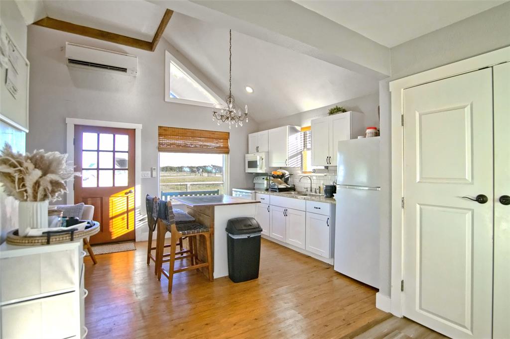 Kitchen featuring white cabinetry, vaulted ceilings with wood-beam detailing, a central island with wood-finish trim, a mounted ductless mini-split system, and a multi-pane wood-finish exterior door
