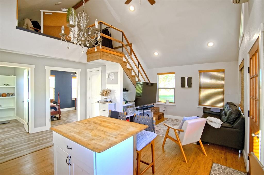 Vaulted ceiling featuring recessed lighting, a wooden loft structure with integrated staircase, chandelier, kitchen island with wood-finish surface, and wood-finish flooring