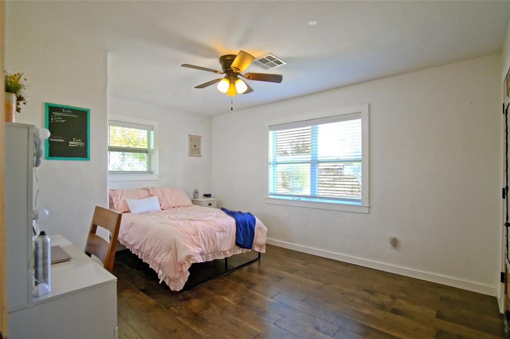 Room featuring wood-finish flooring, dual windows with blinds, and a central ceiling fan with integrated lighting