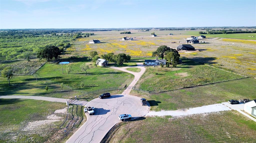 Aerial view of an expansive acreage property featuring a paved cul-de-sac entrance, gated perimeter fencing, mature trees, and an open grass pasture Aerial view of an expansive acreage property featuring a paved cul-de-sac entrance, gated perimeter fencing, mature trees, and an open grass pasture
