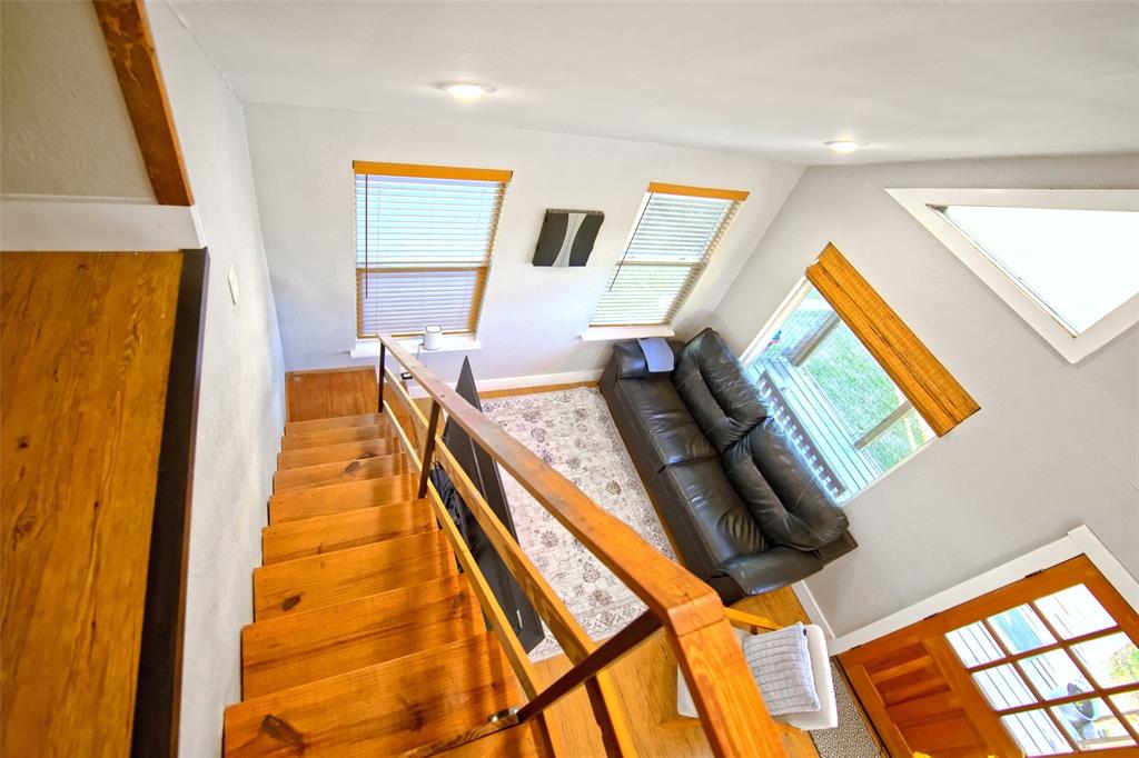 Wood-tread staircase with a structural wood railing, multiple large windows providing natural light, recessed lighting, and a distinct triangular window feature