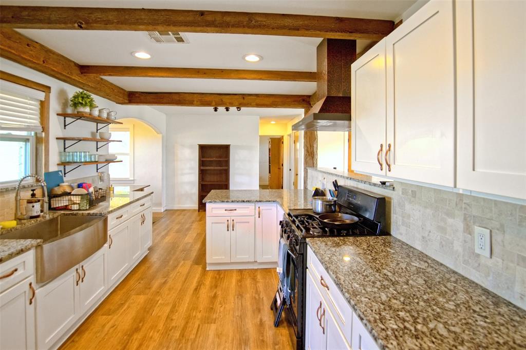 Kitchen featuring white shaker cabinetry, stone countertops, exposed wood ceiling beams, wood-finish flooring, and a stainless steel farmhouse sink