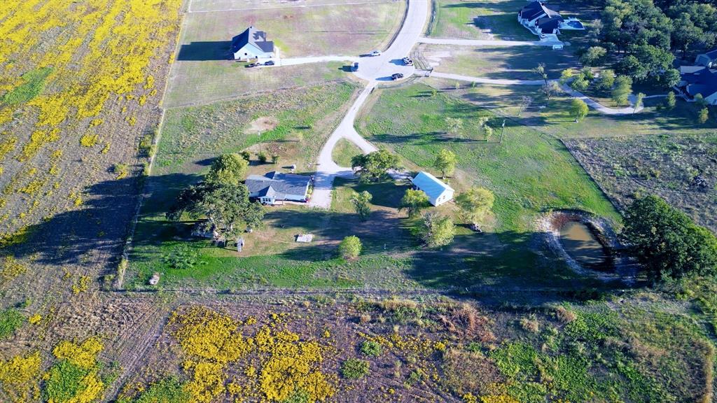 Aerial perspective featuring an expansive lot, paved driveway, detached structure, mature trees, and an on-site pond