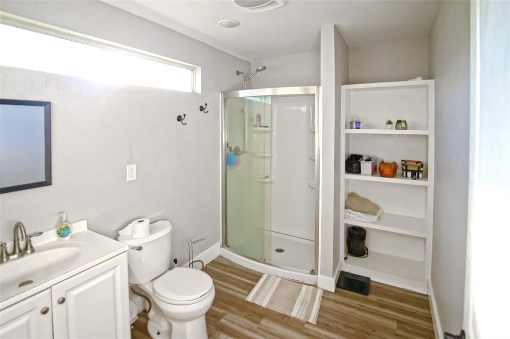 Bathroom featuring wood-finish flooring, a white vanity cabinet with an integrated sink, a glass-enclosed corner shower, built-in recessed shelving, and a clerestory window