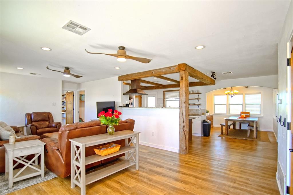 Open-concept interior featuring wood-finish flooring, exposed timber support beams, a stainless steel range hood, recessed lighting, and an arched entryway Open-concept interior featuring wood-finish flooring, exposed timber support beams, a stainless steel range hood, recessed lighting, and an arched entryway