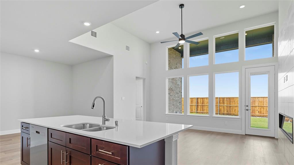 Expansive interior featuring high ceilings, a kitchen island with stone countertops and a dual-basin stainless steel sink, large windows, wood-finish flooring, and a sleek ceiling fan