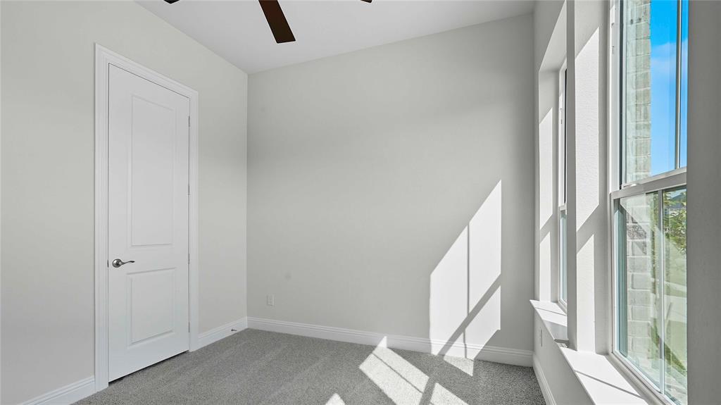 Interior room featuring neutral-toned carpeting, a ceiling fan, a multi-panel interior door with brushed metallic hardware, and tall windows with brick exterior detailing