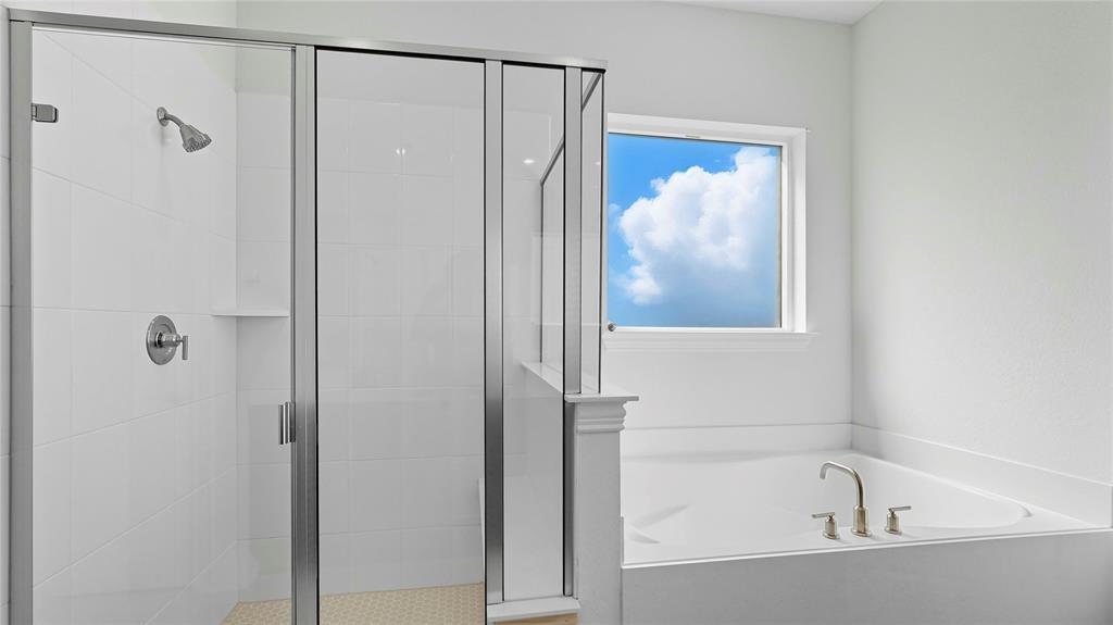 Shower enclosure with polished metal frame and tile surround, accompanied by a soaking tub featuring deck-mounted chrome hardware and a window inset