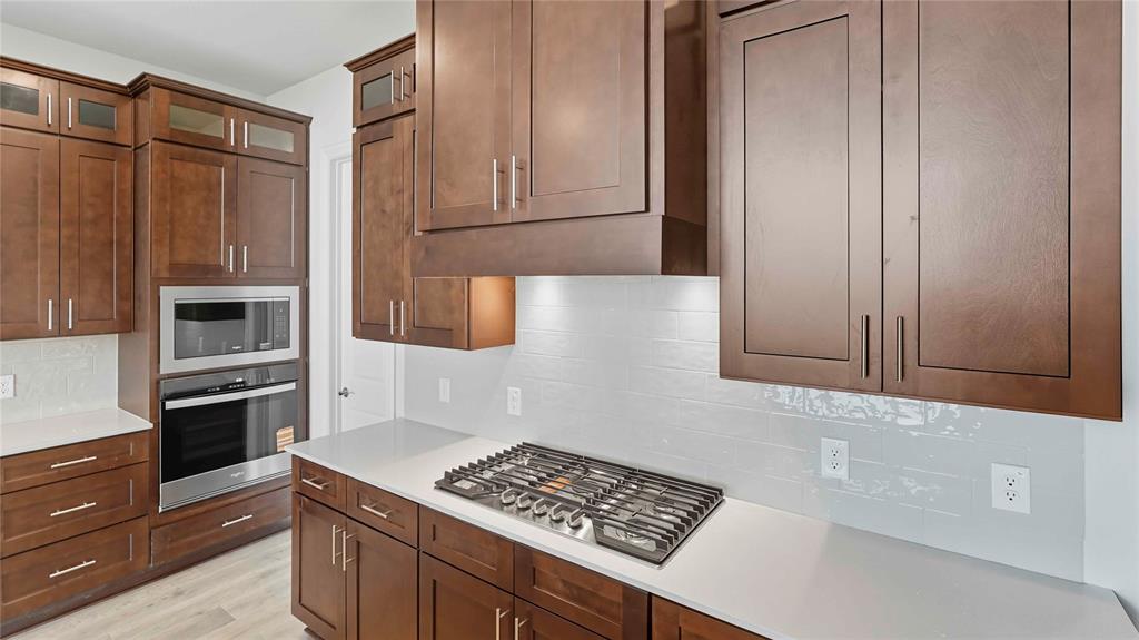 Kitchen featuring dark-finish cabinetry, light-toned stone-surface countertops, a tile backsplash, a built-in stainless steel double oven, and a gas cooktop