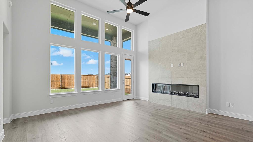 High-ceiling room featuring large floor-to-ceiling windows, wood-finish flooring, a full-height tile fireplace surround with a linear insert, and a ceiling fan