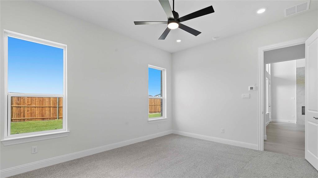 Neutral-toned interior featuring plush carpeting, a modern matte black ceiling fan, recessed lighting, and large windows providing natural light