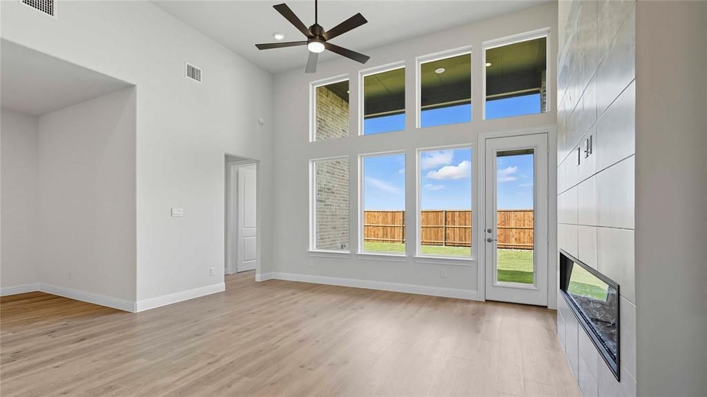 High-ceiling living area featuring wood-finish flooring, a wall-mounted fireplace with large-format tile surround, multiple rows of oversized windows, and a dedicated ceiling fan