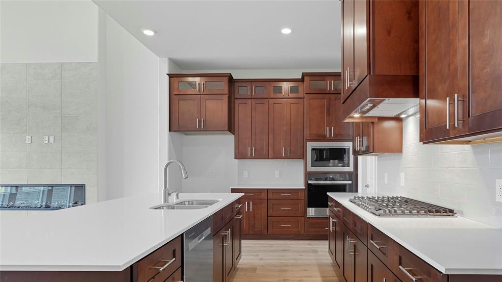 Kitchen featuring custom stained-wood cabinetry, white stone countertops, built-in stainless steel double wall ovens, a gas cooktop, and wood-finish flooring