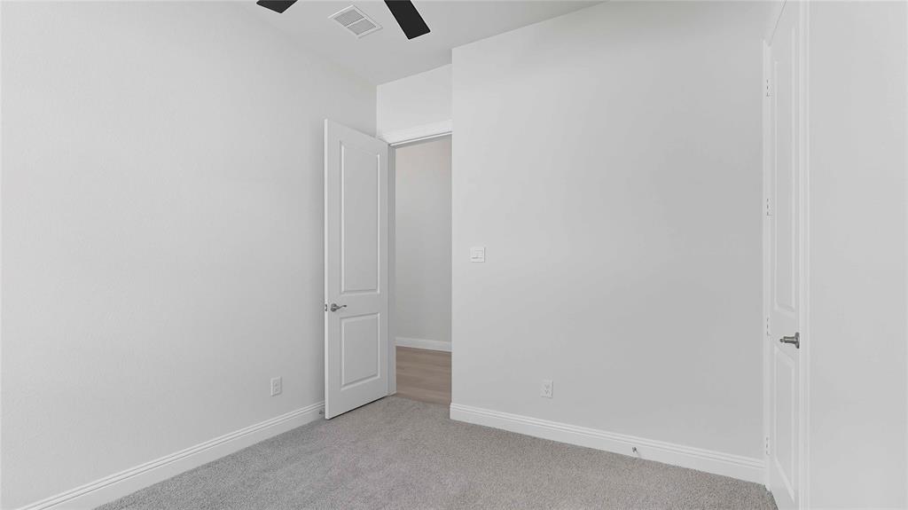 Interior space featuring neutral wall tones, plush wall-to-wall carpeting, and a ceiling-mounted matte black fan, accented by solid-core paneled doors with brushed nickel hardware