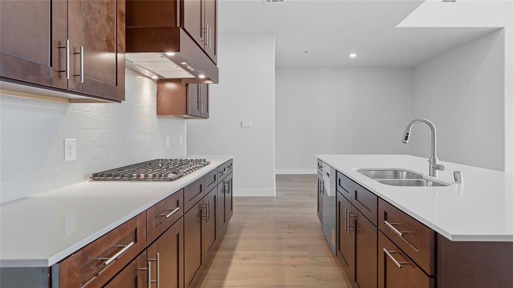 Kitchen featuring dark-toned cabinetry, solid-surface countertops, a white subway-tile backsplash, an integrated gas cooktop, and an island with an undermount double-basin sink