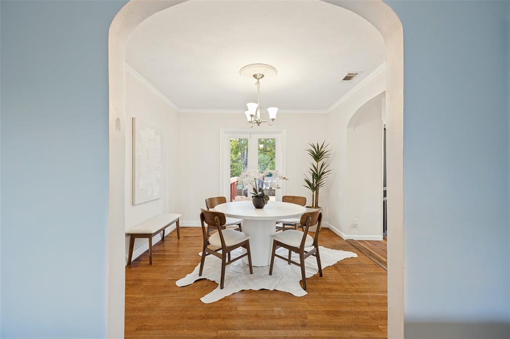 Arched doorway entry into a room featuring wood-finish flooring, crown molding, a central ceiling medallion with a multi-light fixture, and glass-paned doors
