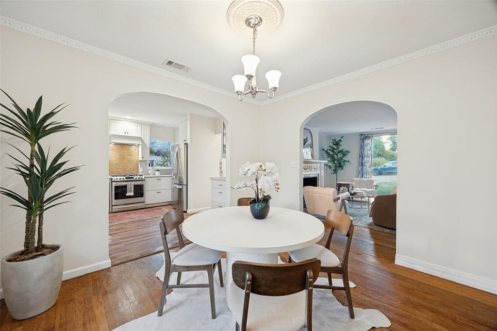 Dining area featuring arched entryways, wood-finish flooring, crown molding, and a decorative ceiling medallion with a three-light chandelier