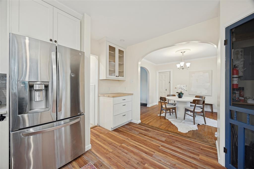 Kitchen featuring white cabinetry with glass-front display uppers, wood-finish flooring, and stainless steel refrigerator