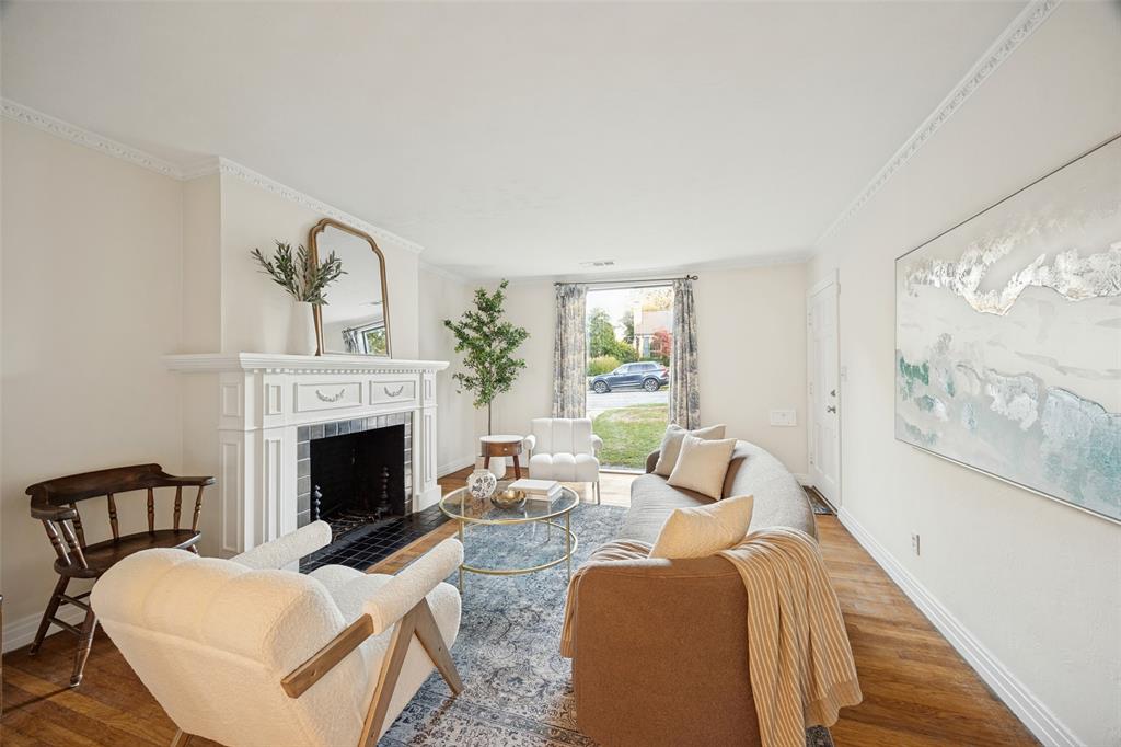 Living area featuring wood-finish flooring, crown molding, and a fireplace with a white mantel and tile hearth