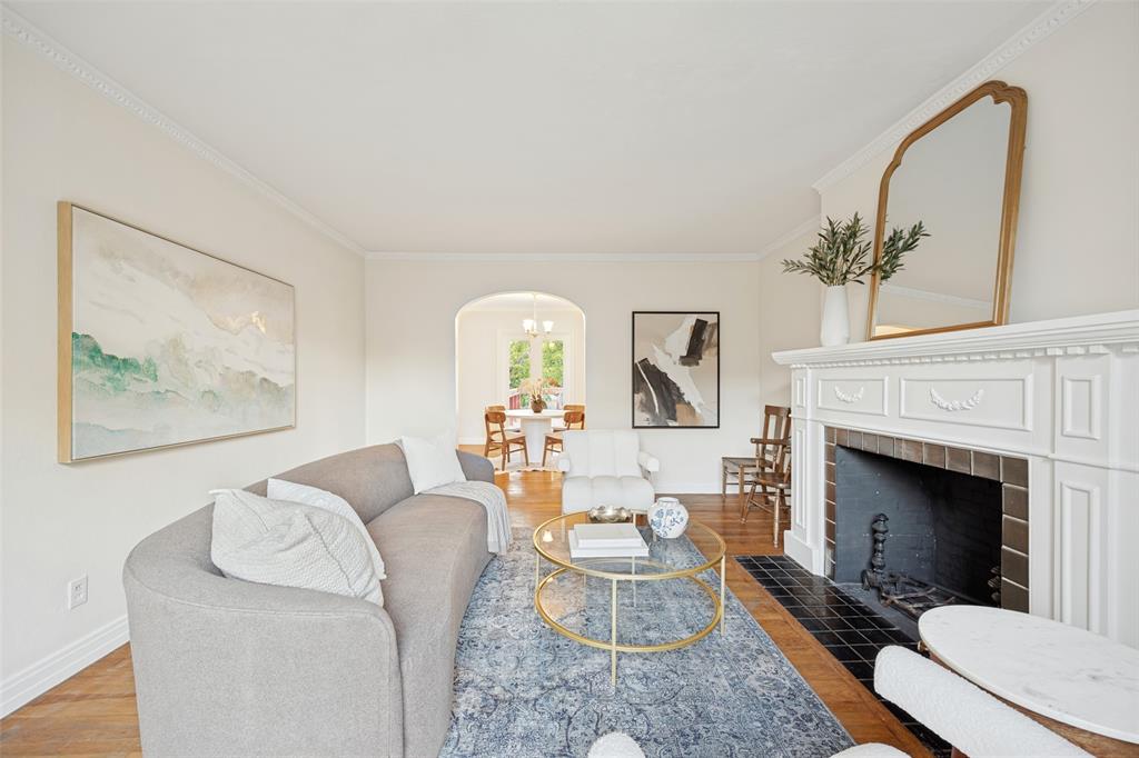 Living area featuring wood-finish flooring, a traditional white fireplace mantel, black tile hearth, and arched architectural detailing