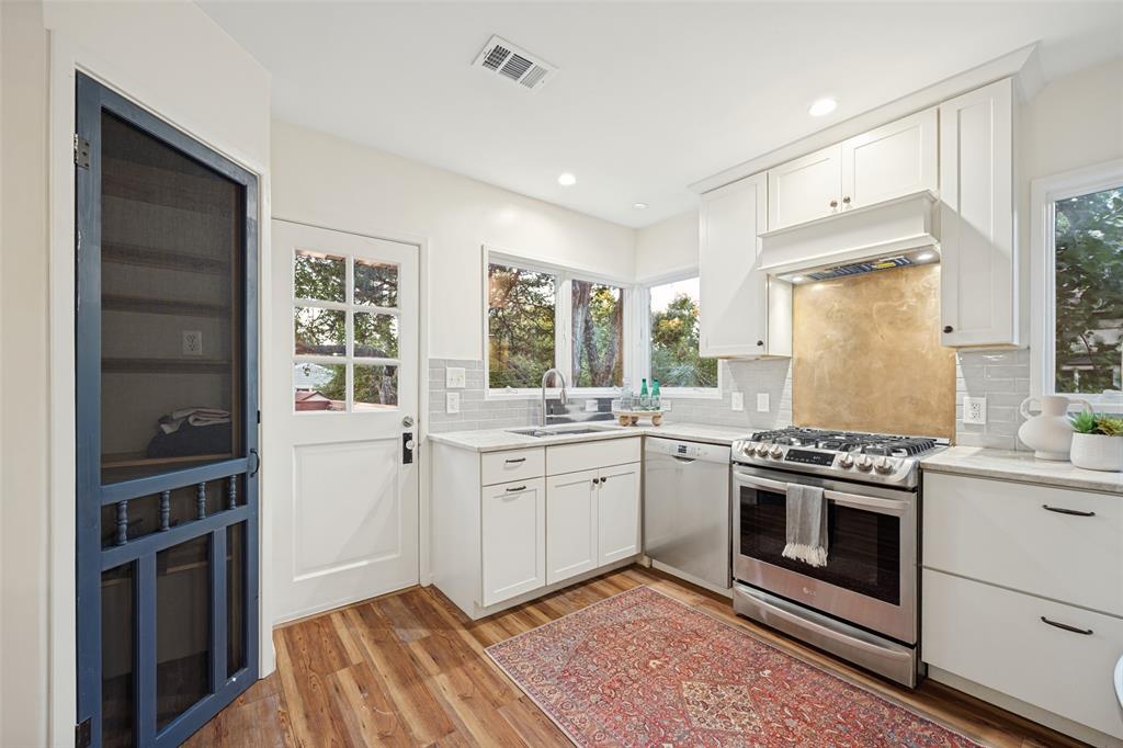 Kitchen featuring shaker-style cabinetry, stainless steel appliances, stone-finish countertops, subway tile backsplash, and wood-finish flooring