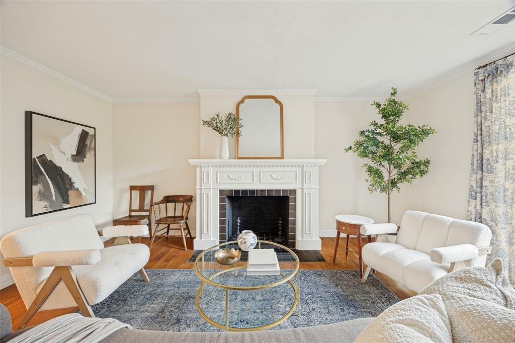 Living area featuring a classic fireplace with white millwork surround, crown molding, and wood-finish flooring