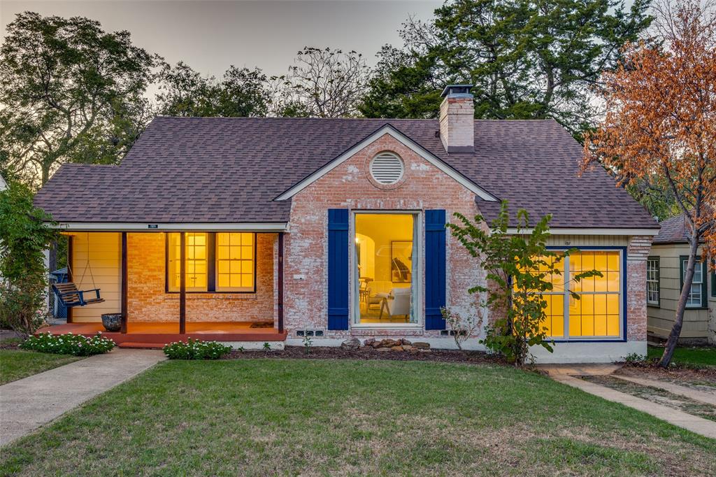 Exterior facade featuring white-washed brick, a covered front porch, a prominent brick chimney, decorative blue shutters, and multi-pane windows