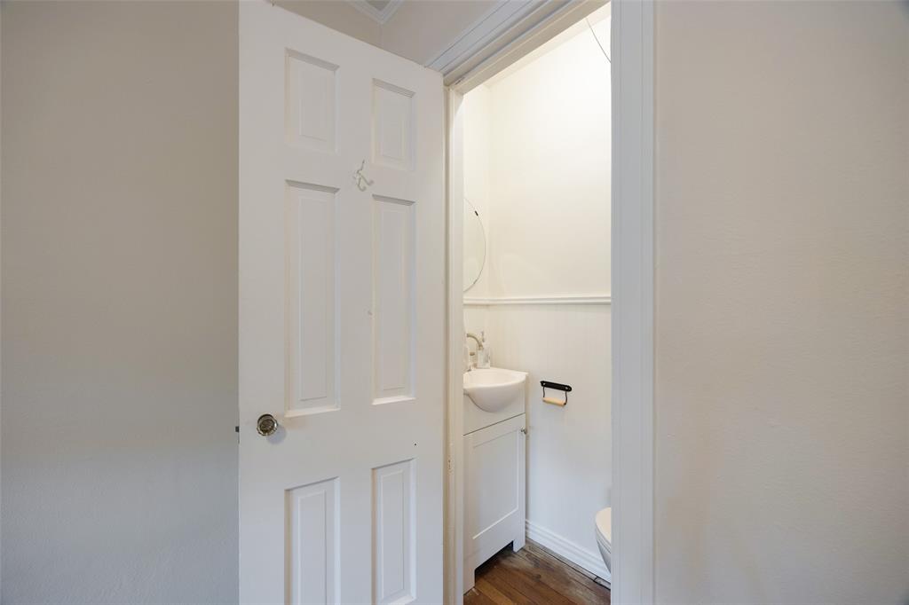 Six-panel interior door with brushed metal hardware opening to a compact vanity featuring a wall-mounted sink, wood-finish flooring, and horizontal wall wainscoting
