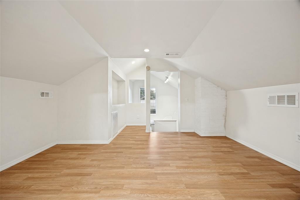 Vaulted ceilings with recessed lighting, wood-finish flooring, built-in shelving, and a painted brick accent wall