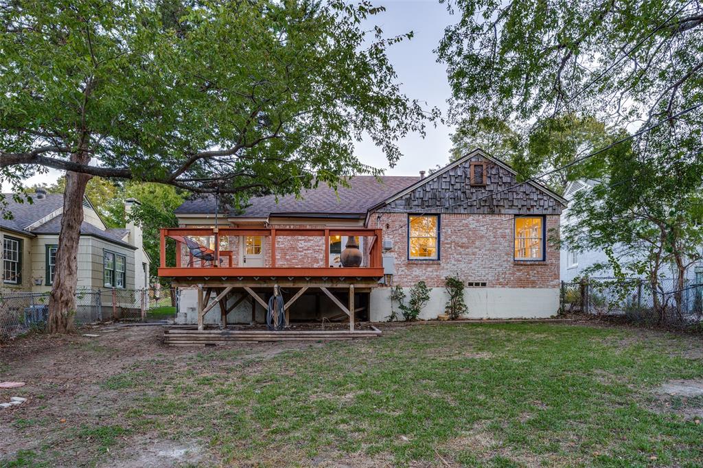 Rear exterior featuring a brick facade with shingle-style siding, an elevated wood deck, and a fenced backyard