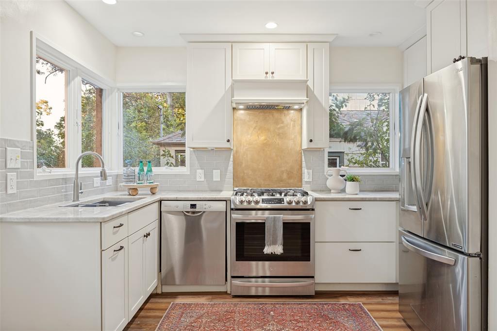 Kitchen featuring white cabinetry, stainless steel appliances, light-toned countertops, subway tile backsplash, and a metallic range backsplash