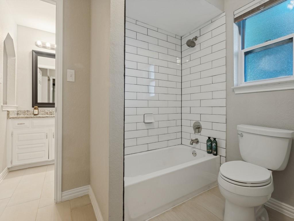 Bathroom featuring a white subway tile shower surround, tub with chrome fixtures, and stone-finish vanity countertop